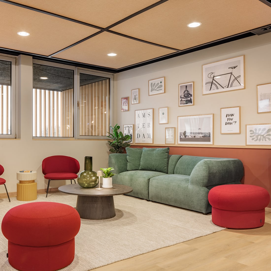 A stylish hotel lounge with green sofa, red ottomans, and framed art on the wall.